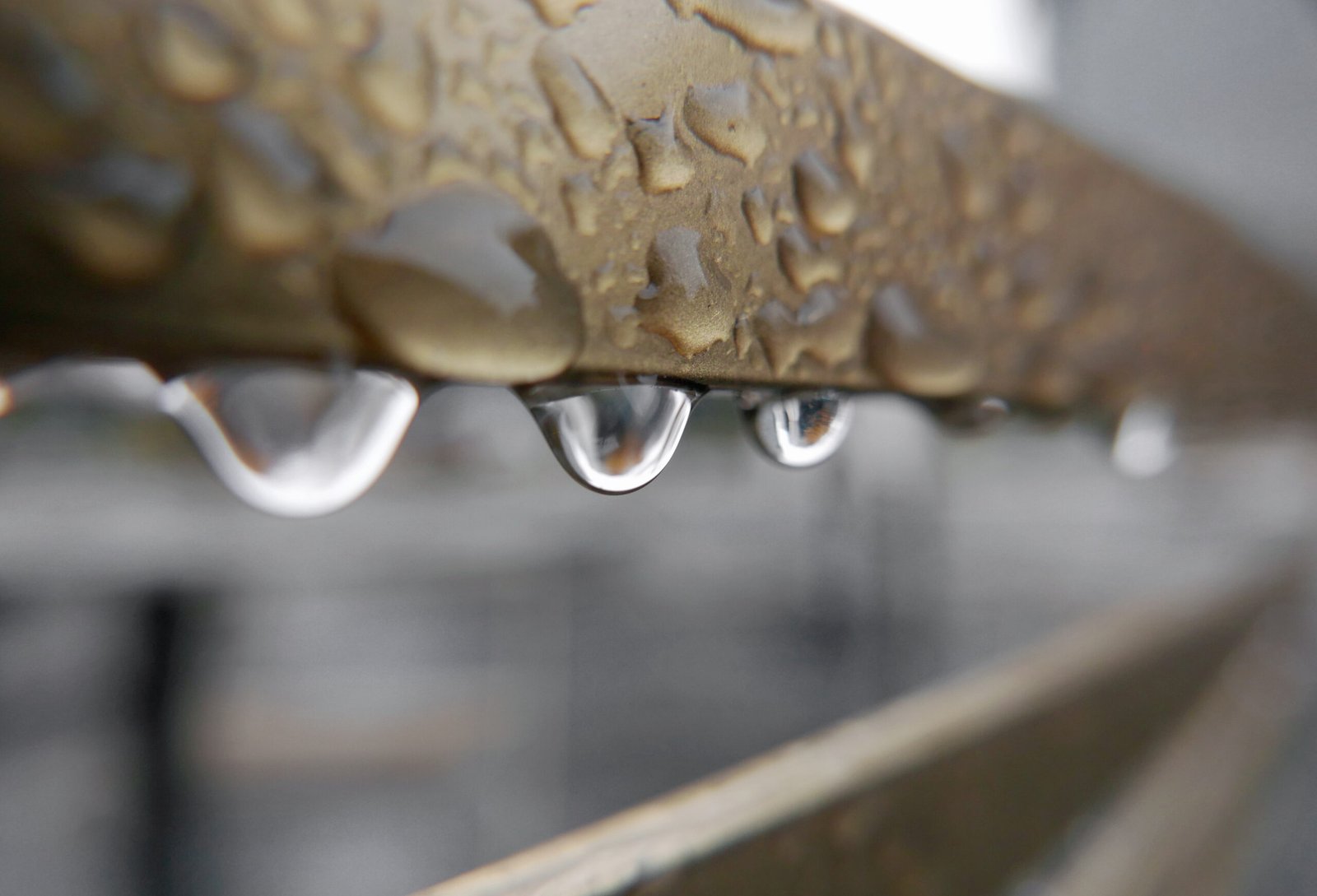Wassertropfen hängen von feuchtem Metallprofil eines Balkons nach unten